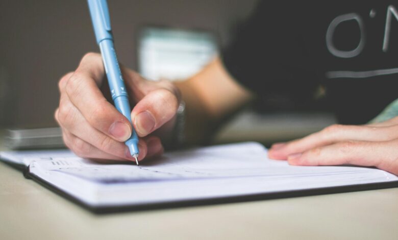 person holding blue ballpoint pen writing in notebook